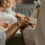 Elderly couple holding hands during a cozy family gathering indoors.